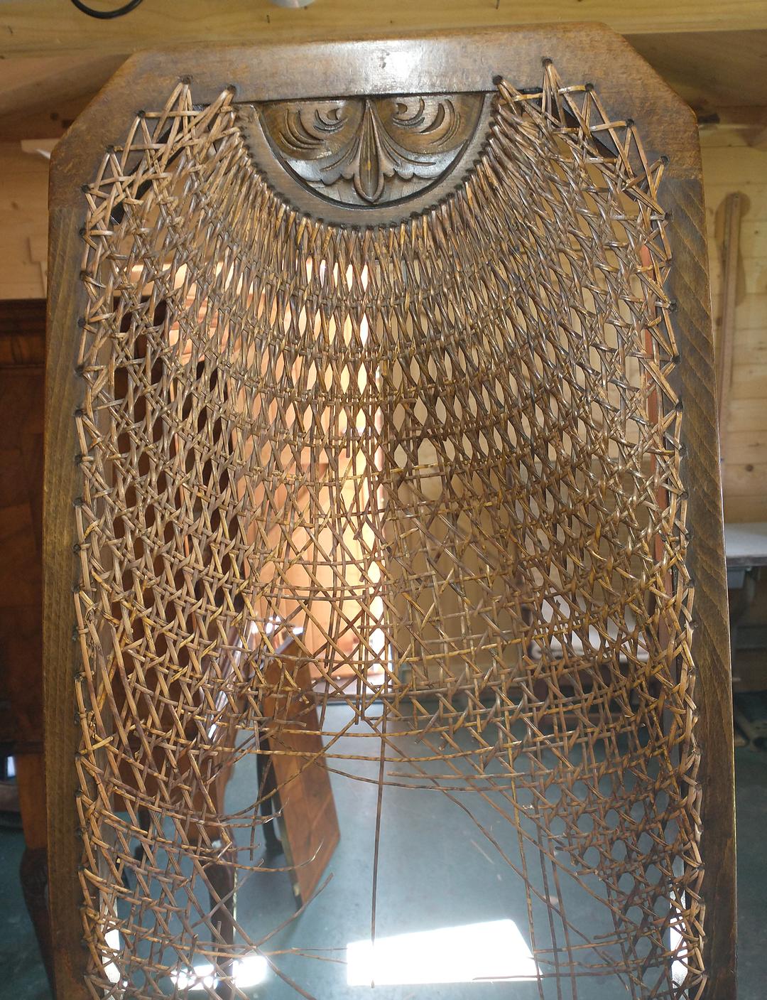 A caned chair back with a large section of cane broken and hanging loose, before recaning