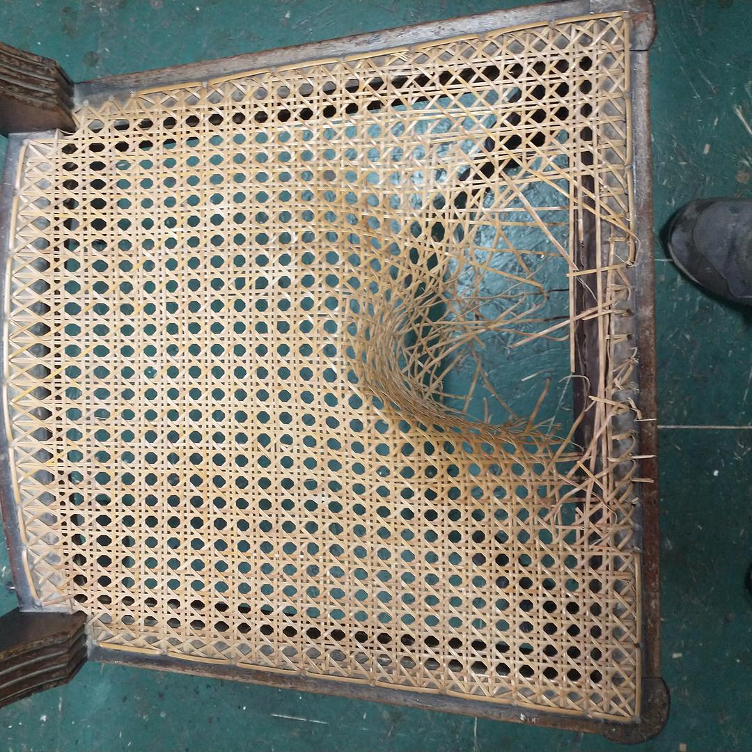 Top view of a hand-caned seat that has been sat through, with a sagging, broken hole