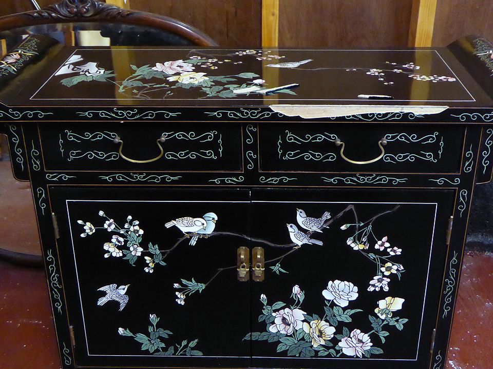 Black lacquer cabinet with bird and flower decoration and a chipped top edge, before repair
